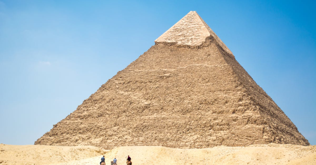 Iconic Giza Pyramid with riders on camels under bright daylight, capturing Egyptian desert landscapes.